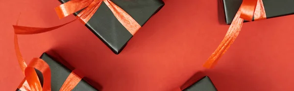 Top view of black gift boxes with bows and ribbons on red background, panoramic shot — Stock Photo