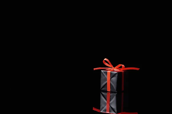 Black decorative gift with red ribbon isolated on black — Stock Photo