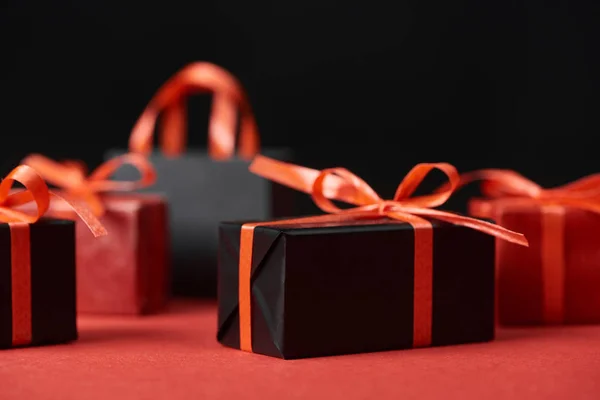 Foco seletivo de presentes com fitas vermelhas e saco de compras isolado em preto — Fotografia de Stock