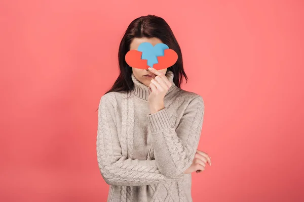 Frau verdeckt Gesicht und hält blaues und rotes Papier mit gebrochenem Herzen auf rosa — Stockfoto