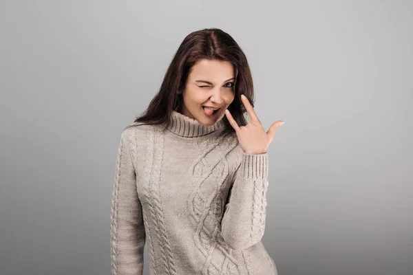 Cheerful woman showing rock sign while sticking out tongue isolated on grey — Stock Photo