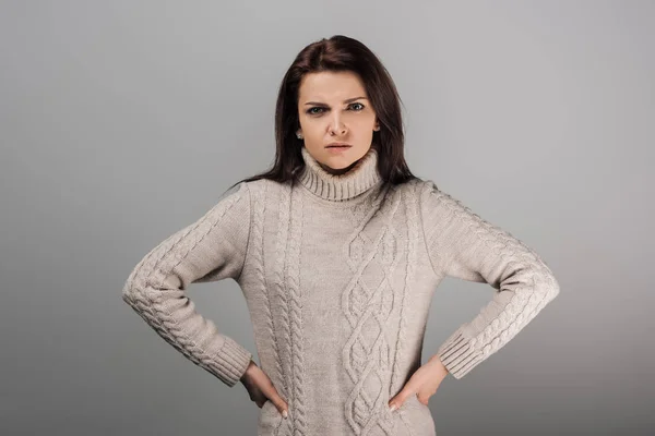 Незадоволена жінка в светрі, що стоїть руками на стегнах ізольована на сірому — стокове фото