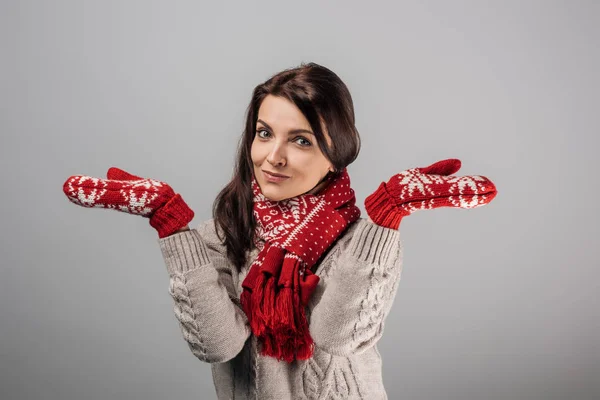 Mulher em luvas vermelhas e cachecol mostrando gesto encolher de ombros isolado em cinza — Fotografia de Stock