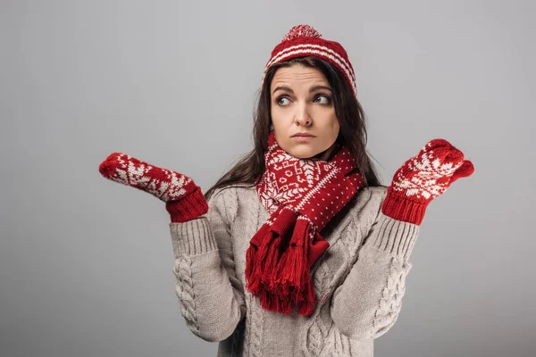 Femme bouleversée en tricot rouge avait, gants et écharpe montrant geste haussement d'épaules isolé sur gris — Photo de stock