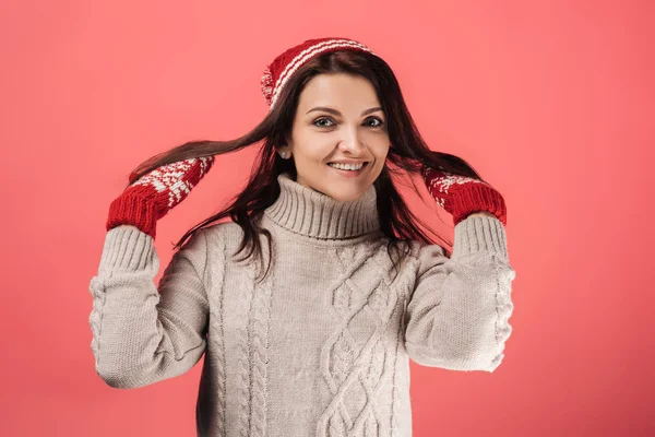 Mujer alegre en rojo sombrero de punto y guantes tocando el pelo en rosa - foto de stock