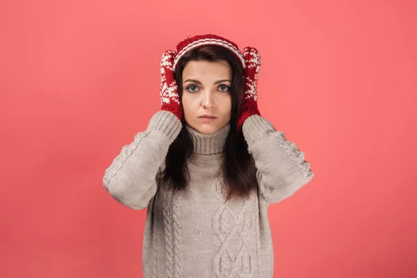 Attractive woman in knitted hat and gloves covering ears on pink — Stock Photo