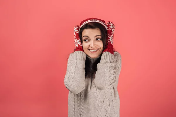 Happy woman in knitted hat and gloves covering ears on pink — Stock Photo