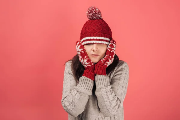 Femme en gants rouges touchant le visage et couvrant les yeux avec un chapeau tricoté sur rose — Photo de stock
