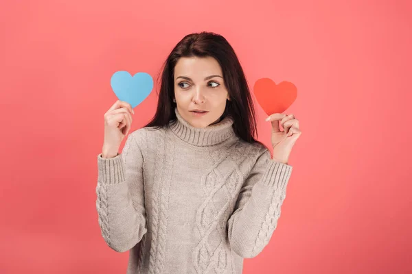 Frau im Pullover hält blaues und rotes herzförmiges Papierkunstwerk auf rosa — Stockfoto