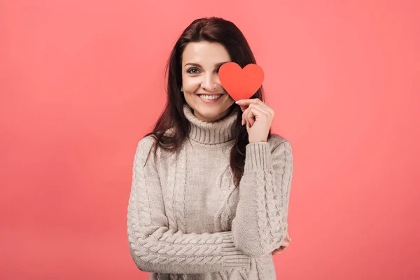 Mujer alegre en suéter caliente sosteniendo papel en forma de corazón cortado en rosa - foto de stock