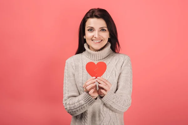 Happy woman in warm sweater holding paper cut with broken heart on pink — Stock Photo