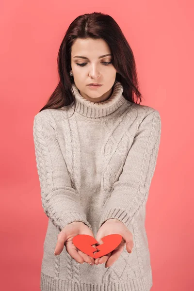 Sad woman in sweater looking at paper artwork with broken heart isolated on pink — Stock Photo