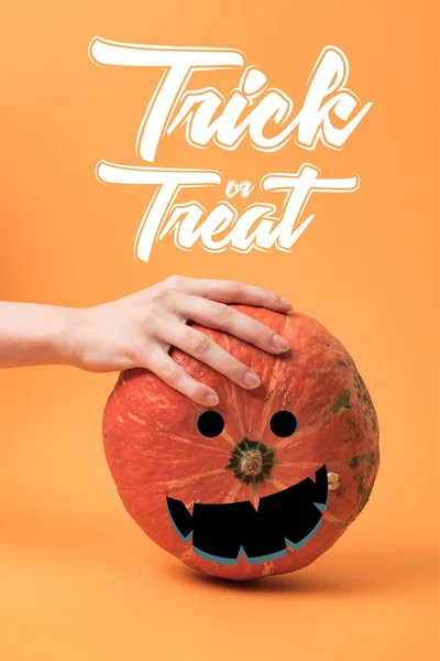 Partial view of woman touching pumpkin on orange background with trick or treat illustration — Stock Photo
