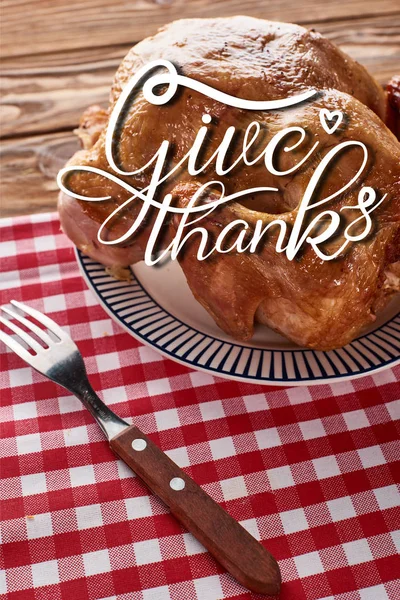 Roasted turkey and fork served on red checkered napkin at wooden table for Thanksgiving dinner with give thanks illustration — Stock Photo