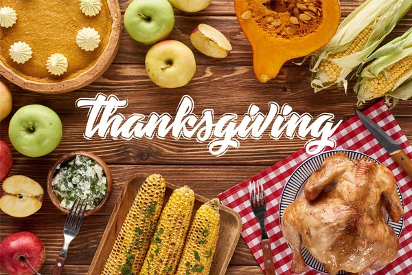 Вид сверху на тыквенный пирог, индейку и овощи, подаваемые за деревянным столом с иллюстрацией к Дню благодарения — стоковое фото