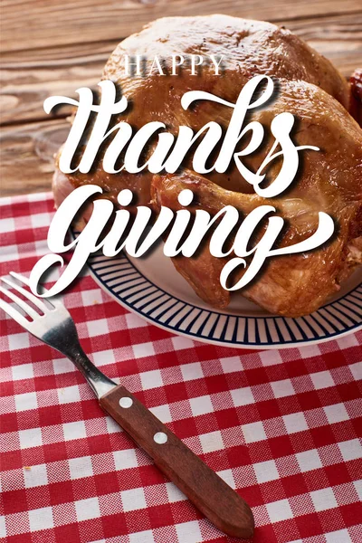 Roasted turkey and fork served on red checkered napkin at wooden table with thanksgiving illustration — Stock Photo