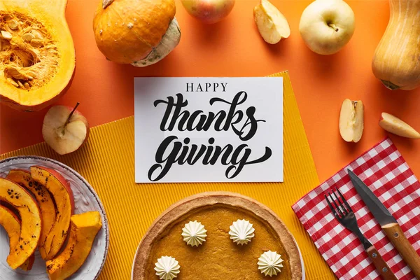 Top view of pumpkin pie, ripe apples and happy thanksgiving card on orange background — Stock Photo