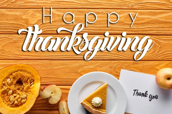 Вид сверху на тыквенный пирог, спелые яблоки и благодарственная открытка на деревянном столе с счастливой иллюстрацией Дня благодарения — стоковое фото