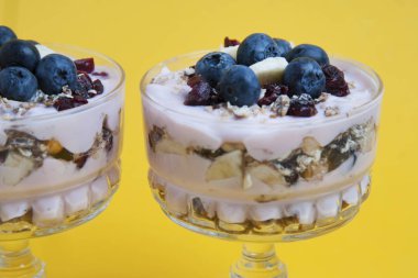 Cam bardakta Servis Kahvaltı. Granola oatmeals, kurutulmuş meyve, yaban mersini ve yoğurt ile kapatın. Isoalted sarı tahtası üzerinde.