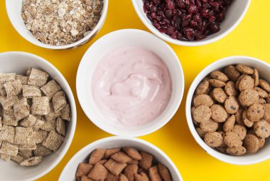 Bütün tahıl müsli, kurutulmuş meyve, granola ve daire içinde düzenlenmiş oatmeals kâse. Sarı arka plan üzerinde izole.