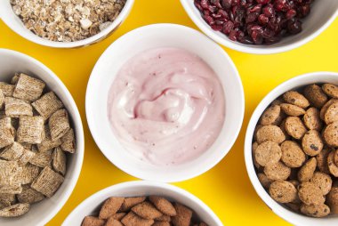 Bütün tahıl müsli, kurutulmuş meyve, granola ve daire içinde düzenlenmiş oatmeals kâse. Sarı arka plan üzerinde izole.
