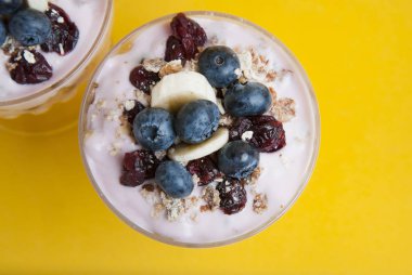 Cam bardakta servis kahvaltı. Granola yulaf yemek, kuruyemiş, yaban mersini ve yoğurt ile. Sarı arka plan. İzole.