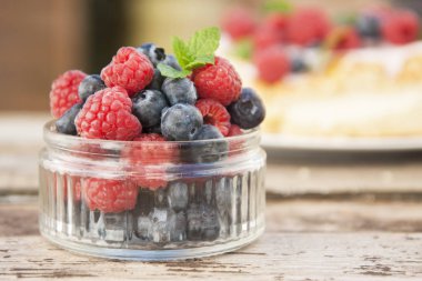 Küçük cam kase yaban mersini ve ahududu, yemek hazır dolu rustik tahtaya yerleştirilir.