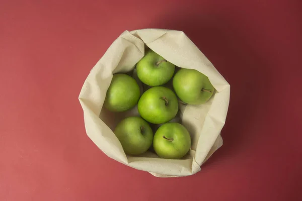 Bio fruit - green apples in white tote canvas fabric. Eco bag, shopping sack on red background. Zero waste concept.