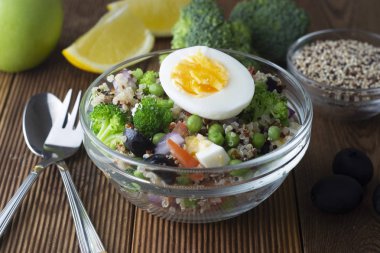 Quinoa ve farklı sebze - yumurta, brokoli, domates, yeşil bezelye, kırmızı soğan ile top. Ahşap masa.