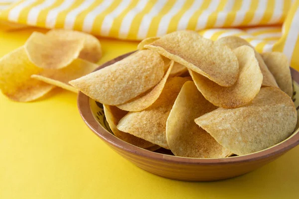 Potato chips in bowl on yellow background, top view