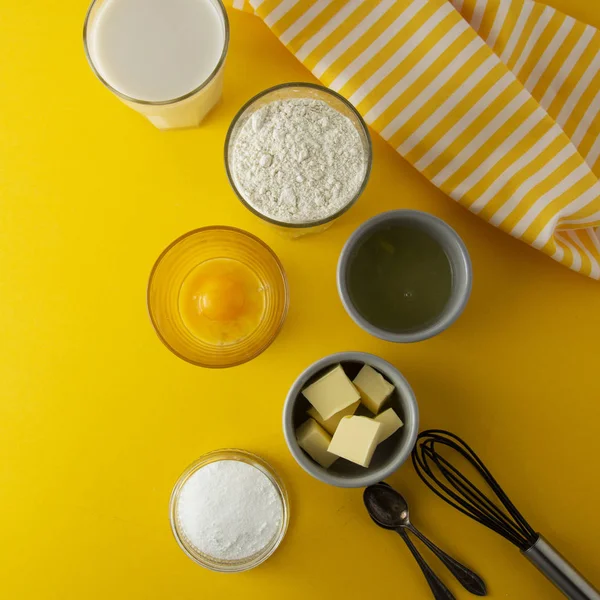 Ingredients for baking pastry or dessert - butter, flour, eggs, milk, sugar. Yellow background, flat lay. Dessert recipe, cooking process.