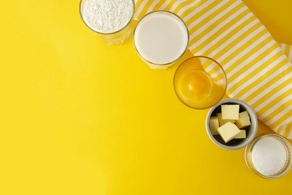 Ingredients for baking pastry or dessert - butter, flour, eggs, milk, sugar. Yellow background, flat lay. Dessert recipe, cooking process. Copy space.