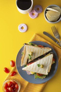 Atıştırmalıklar, fast food konsepti. İş yerinde yemek yiyor. Taze sossandviç, sebze, kahve, patates cipsi, tatlı kurabiye. Tablet ekranı. Sarı arka plan.