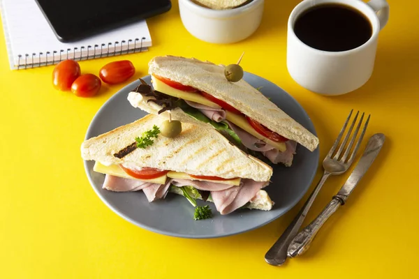 Snacks, concepto de comida rápida. Comer en el trabajo. Sandwich de club fresco, verduras, café, papas fritas, galletas dulces. Pantalla de tableta. Fondo amarillo . — Foto de Stock