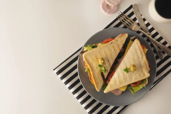 Homemade sandwich. Toasted double panini with ham, cheese fresh vegetables. Snack at work or lunch. Light background.