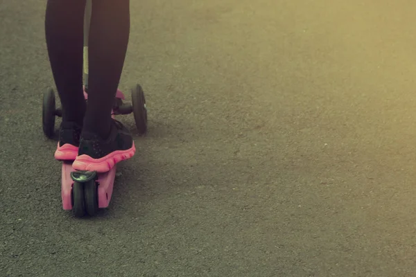 Una bambina che cavalca uno scooter nel parco. Educazione, concetto genitoriale. Copia spazio . — Foto Stock