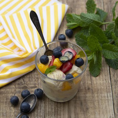 Dondurma ile meyve salatası - yaban mersini, çilek, mango ve nane, yaz ferahlatıcı tatlı. Ahşap arka plan. Vanilyalı dondurma ile Cam.