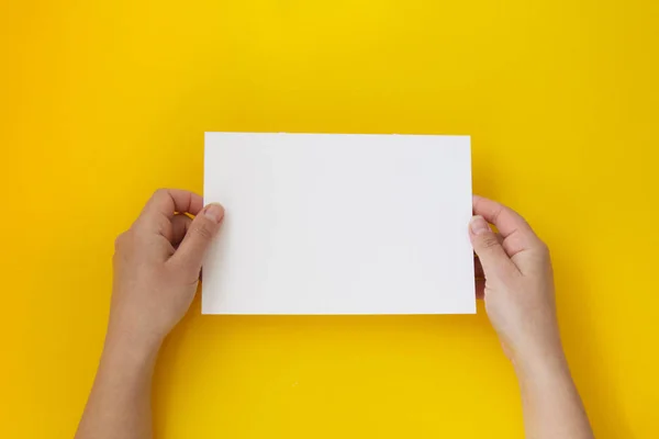 Hands holding blank white, empty paper isolated on yellow with copy space Stock Picture