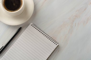 Mermer masada bir fincan kahve içeren açık defter. İş yeri, çalışma masası. Üstte görüntü.