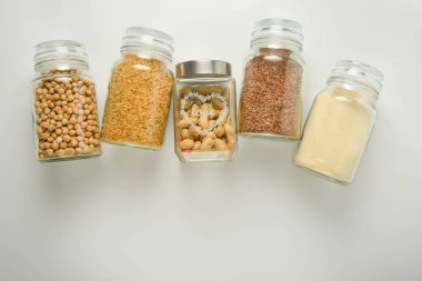 Cam kavanozda çeşitli çiğ tahıllar. Sıfır atık kavramı. Yiyecek deposu. Düz yatıyordu. Beyaz arka plan.