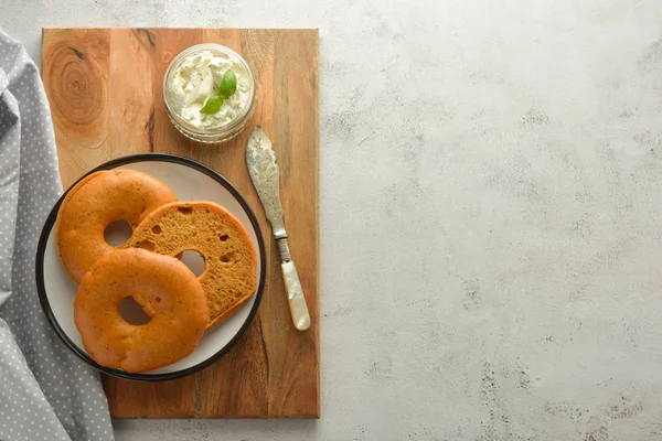 Heerlijke bagels met roomkaas op houten bord, gebak brood voor het ontbijt. Bovenaanzicht. Ruimte kopiëren. — Stockfoto