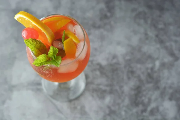 Um cocktail de Verão. Suco de laranja com hortelã, xarope, fatias de frutas e cereja com gelo. Fundo escuro . — Fotografia de Stock