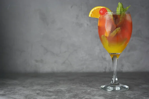 Cocktail estivo. Succo d'arancia con menta, sciroppo, fette di frutta e ciliegia con ghiaccio. Sfondo scuro . — Foto Stock