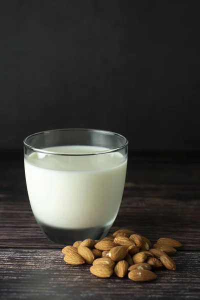 Almond milk - alternative to clasic milk. A glass with almond milk and almond nuts. Dark food photo with copy space. Healthy, vegan milk.