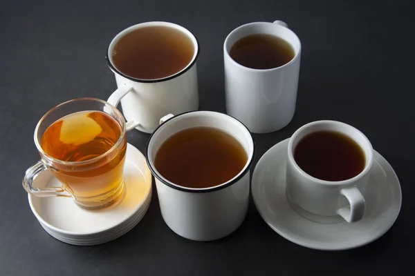 Top view of various cups, mugs with hot tea drink on dark background, copy space. Tea time or tea brake. Autumn beverage. Toned image with tea cups.