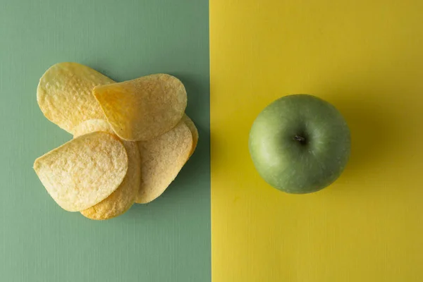 Sağlıksız karşı sağlıklı gıda. Choise kavramı. Patates cipsi veya atıştırmalık için yeşil elma. Üst görünüm, renkli arka plan.