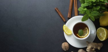 Koyu arka planda limon ve nane yaprakları ile zencefil çayı Fincan. Banner, soğuk ve sonbahar saati.