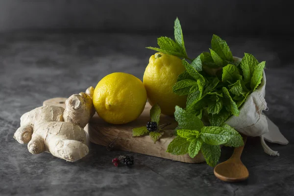 Ginger, lemons and mint leaves on dark background. Ginger tea, drink ingredients, cold and autumn time.