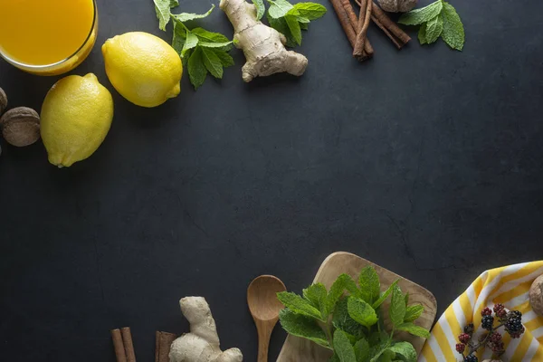 Ginger, lemons and mint leaves on dark background. Ginger tea, drink ingredients, cold and autumn time. Copy space.