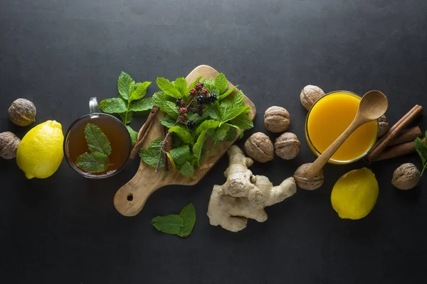 Taza de té de jengibre con limones y hojas de menta sobre fondo oscuro. Té de jengibre, ingredientes de bebidas, tiempo frío y otoño . — Foto de Stock